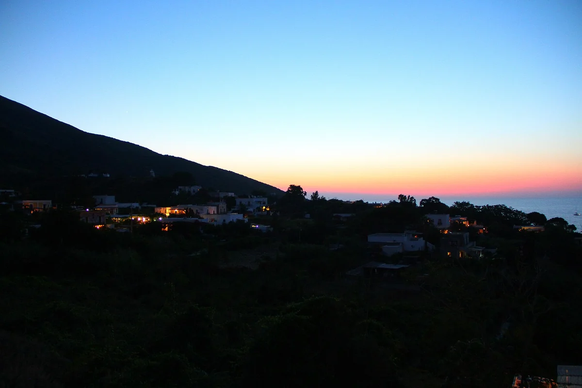 Sunset over Stromboli village with the dark volcano cone behind, Aeolian Islands, Italy